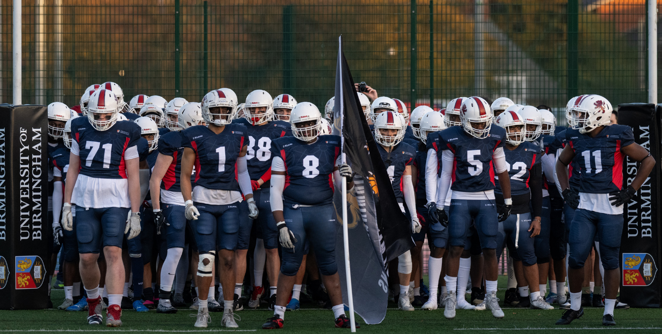 UoB American Football - Birmingham Lion stood in a group shot on the pitch, all wearing helmets.
