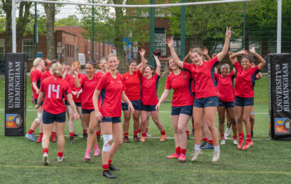 Womens Rugby team cheering after their win, standing in a large group, wearing their red University of Birmingham kit.