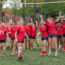 Womens Rugby team cheering after their win, standing in a large group, wearing their red University of Birmingham kit.