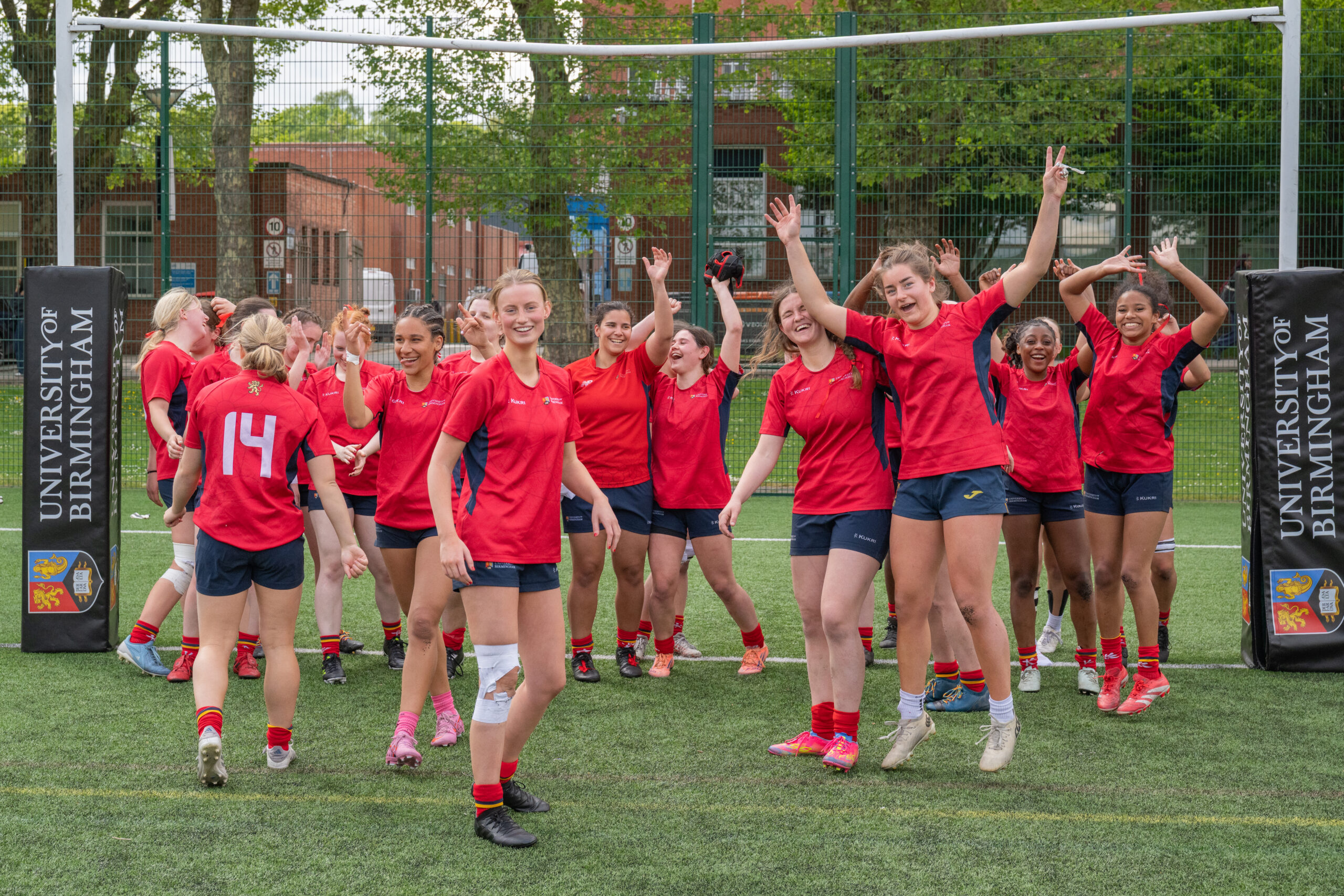 Womens Rugby team cheering after their win, standing in a large group, wearing their red University of Birmingham kit.