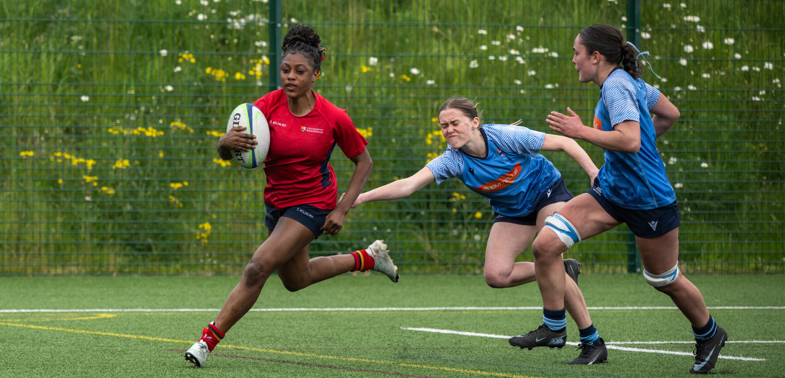 University of Birmingham women's rugby player running with ball and being chased by opponent.