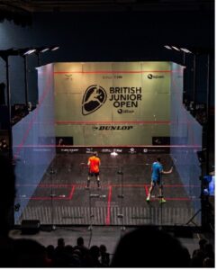 An action shot of two males competing in the British Junior Open in the Glass Court