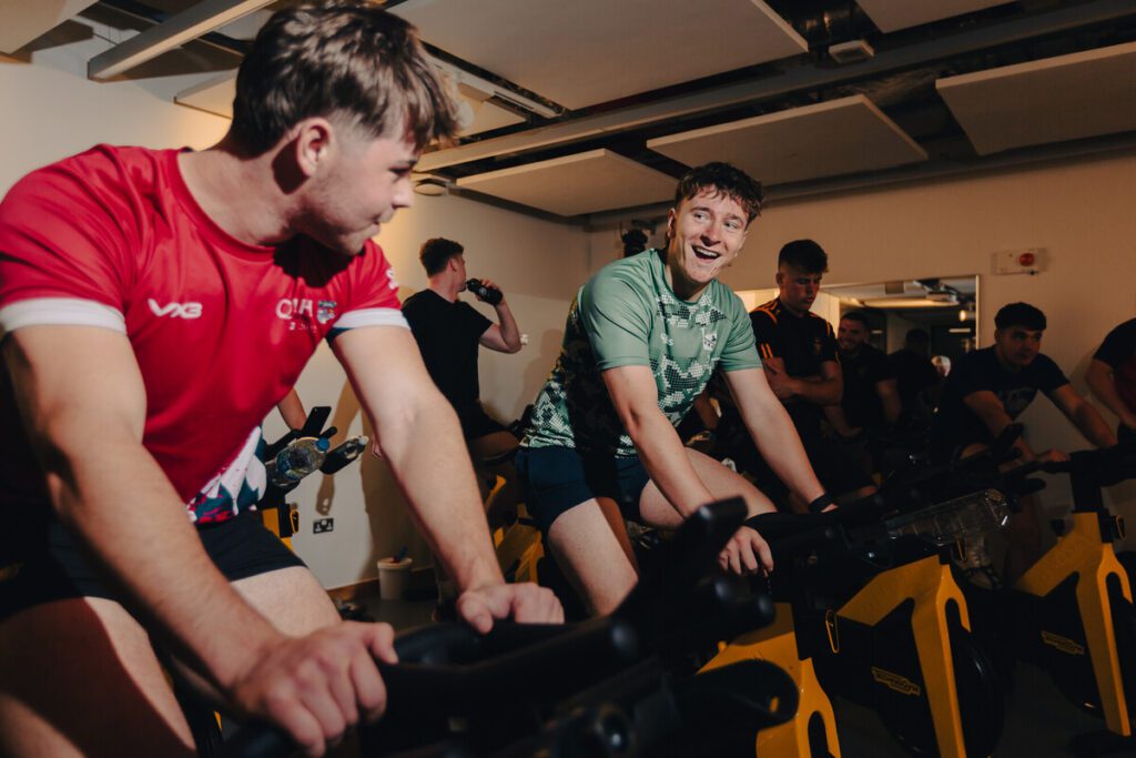 Two students in a studio on cycle/spin bikes.