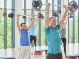two men lifting bars with plates on above their head in a body pump class