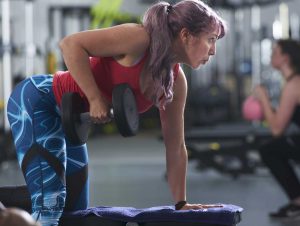 Women with one knee and one hand on a bench pulling a dumbbell towards her