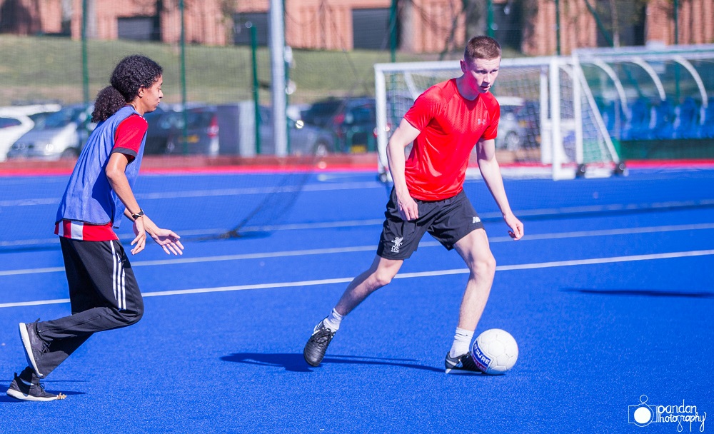 woman and man playing football on a blue football pitch