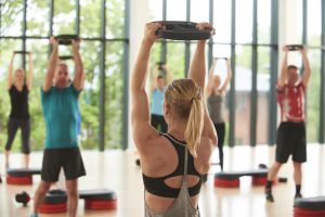 Instructor holding a weight plate above her head for a tricep dip in a Body Pump class