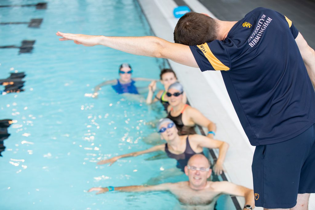 Male teacher demonstrating a stroke to 5 adults in the pool