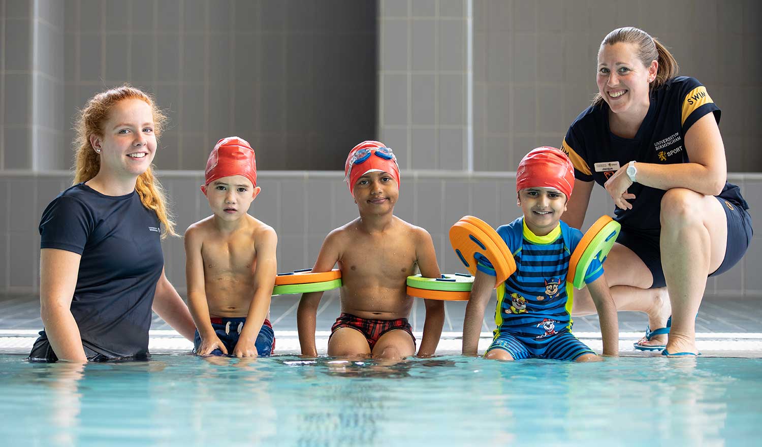 Three juniors and two members of staff sat on the side of the pool