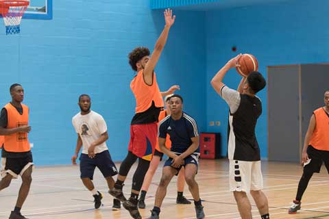 male player shooting a basket with a defending jumping to defend