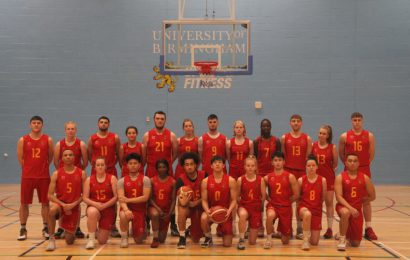 Basketball players from the University of Birmingham pose in front of the basketball hoop in their red match kit