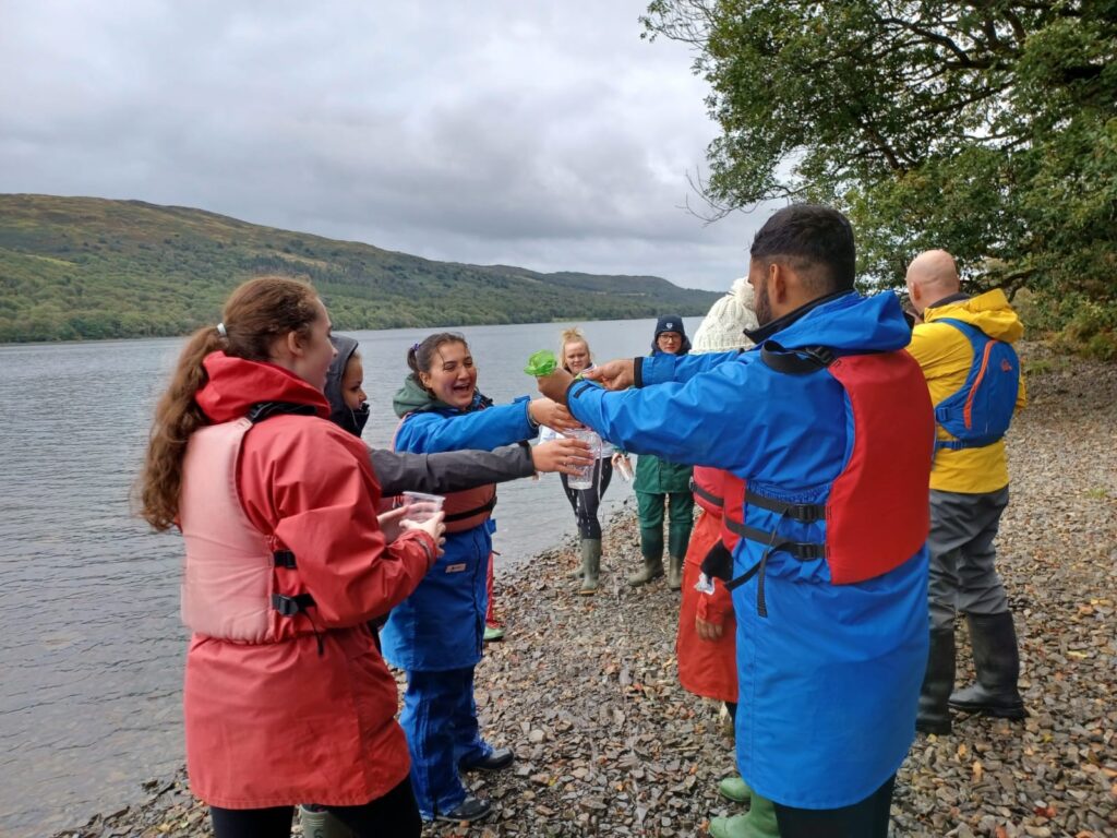 Group of students taking part in an activity by the lake, all wearing waterproofs and life jackets.
