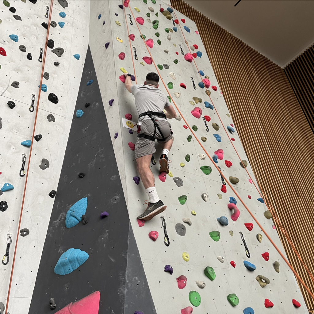 A student climbing towards the top of the climbing wall