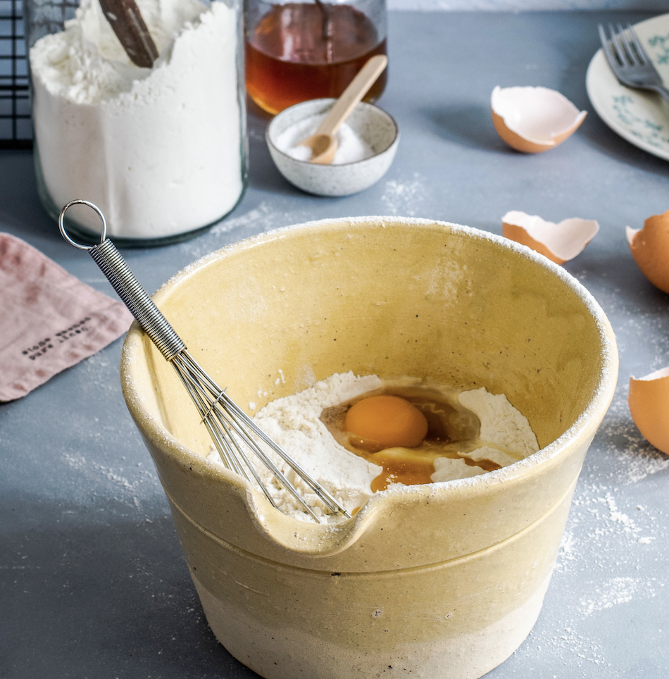 Egg and flour in a mixing bowl with egg shells surrounding bowl