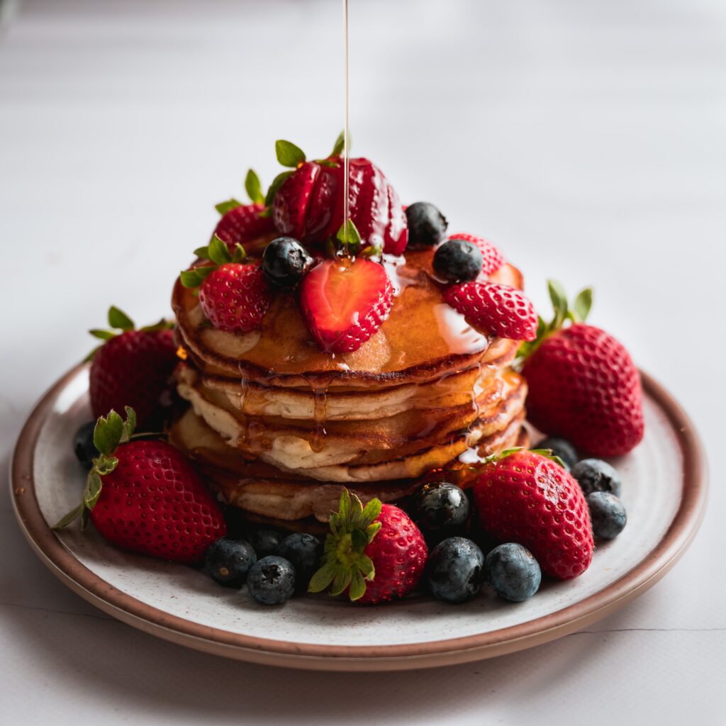 Pancakes drizzled in syrup and covered with strawberries and blueberries