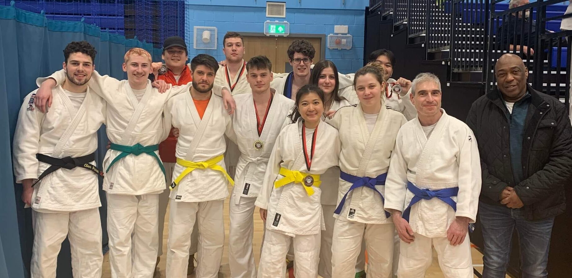 Judo team all in kit smiling for a photo in the Munrow Arena at Sport and Fitness on the Edgbaston campus