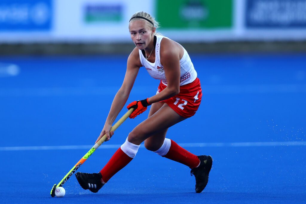 Lily playing Hockey on the blue astroturf hockey pitch at CWG