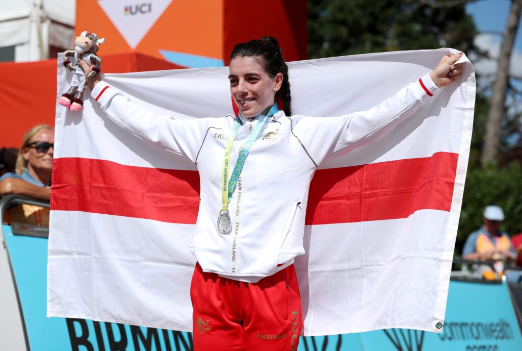 Cyclist Anna with silver medal around neck, holding up England flag