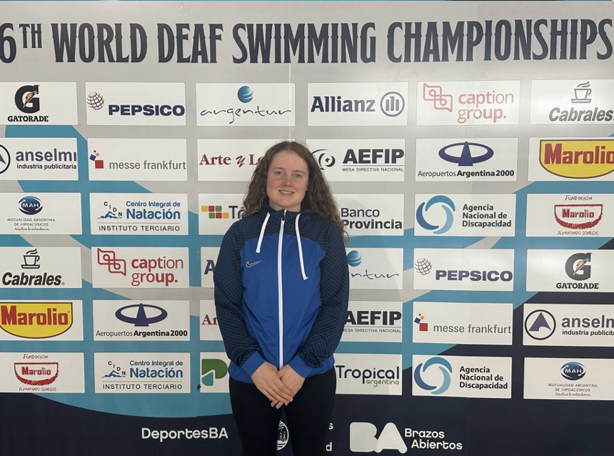 Lucy Jordan-Caws standing infront of World Deaf Swimming Championships board