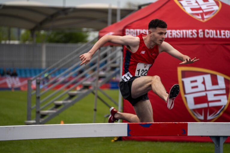 Member of the Athletics team jumping over a hurdle