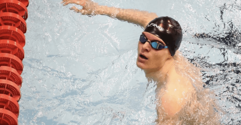 Ollie Morgan in the pool looking up at the camera. Wearing a swimming hat and goggles.