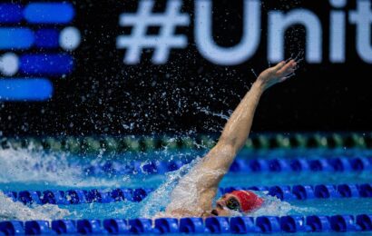 Scholar Ollie Morgan performing the backstroke, arm out of the water wearing a red hat.