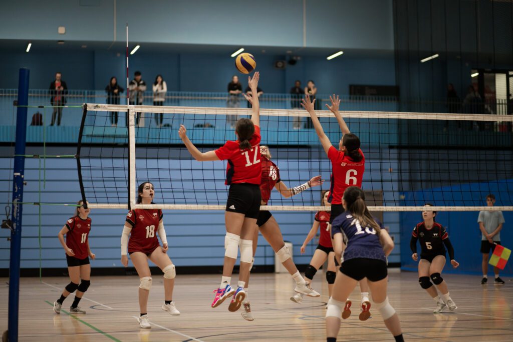 Shot of UOB team playing volleyball. Two members in the air, hitting the ball over the net.