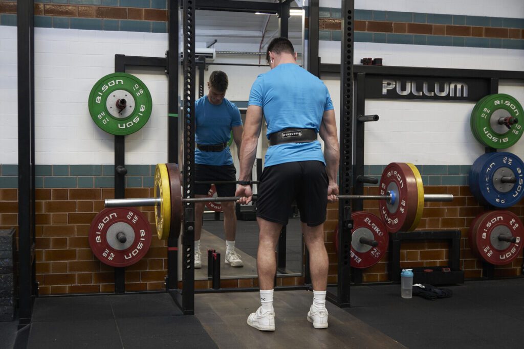 A member working out in Tiverton Gym, lifting weights at the squat rack and stood in front of the mirror.