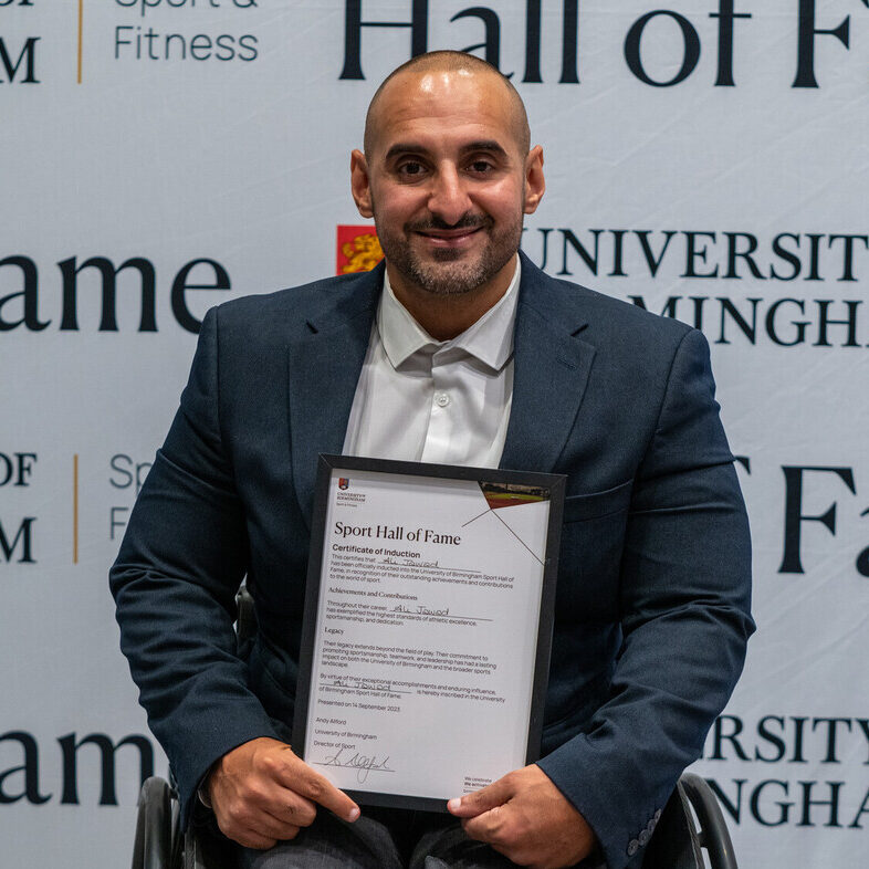 Ali Jawad holding his Sport Hall of Fame award in front of the University of Birmingham Sport & Fitness backdrop.