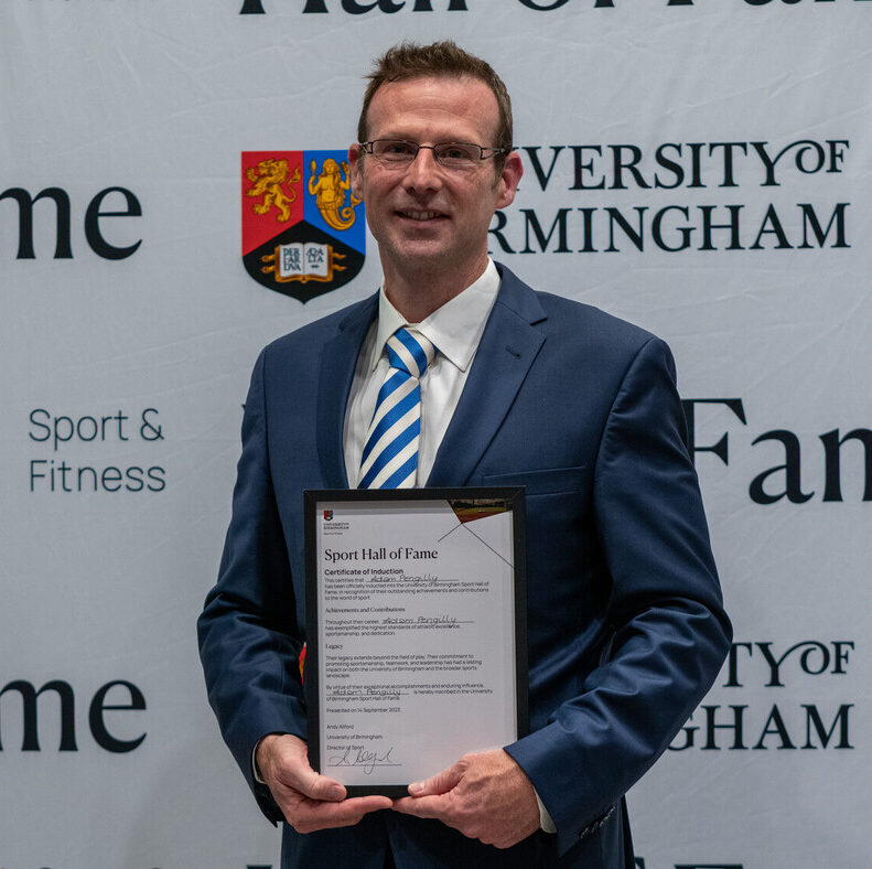 Adam Pengilly with his Hall of Fame Award, standing in front of the Sport of Fitness/Hall of Fame sign.