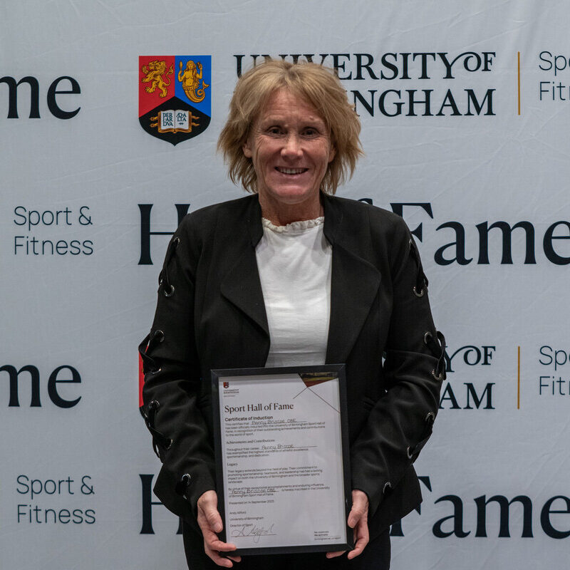 Penny Briscoe holding her Sport Hall of Fame award in front of the University of Birmingham Sport & Fitness backdrop.