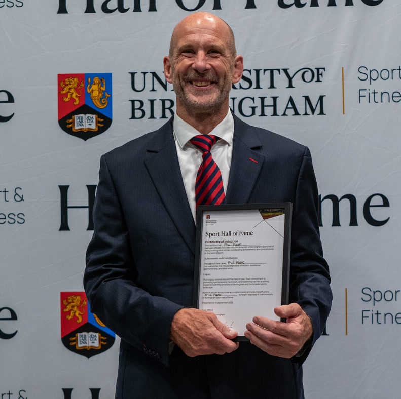 Phil Pask holding his Sport Hall of Fame award in front of the University of Birmingham Sport & Fitness backdrop.