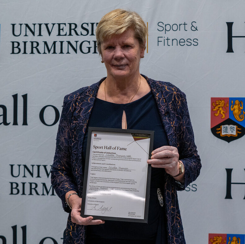 Colette Thomson holding her Sport Hall of Fame award in front of the University of Birmingham Sport & Fitness backdrop.
