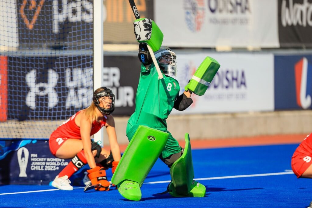 Evie Wood, a hockey goalkeeper, dressed in full kit and helmet on, stood in front of the goal.