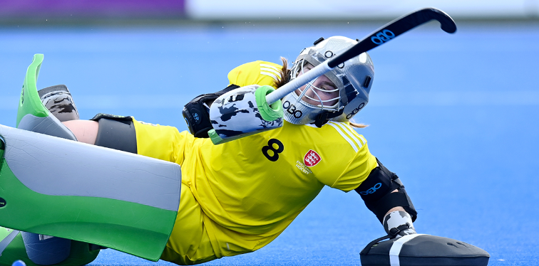 Evie Wood on the floor in her goalkeeping kit, with her hockey stick in the air.