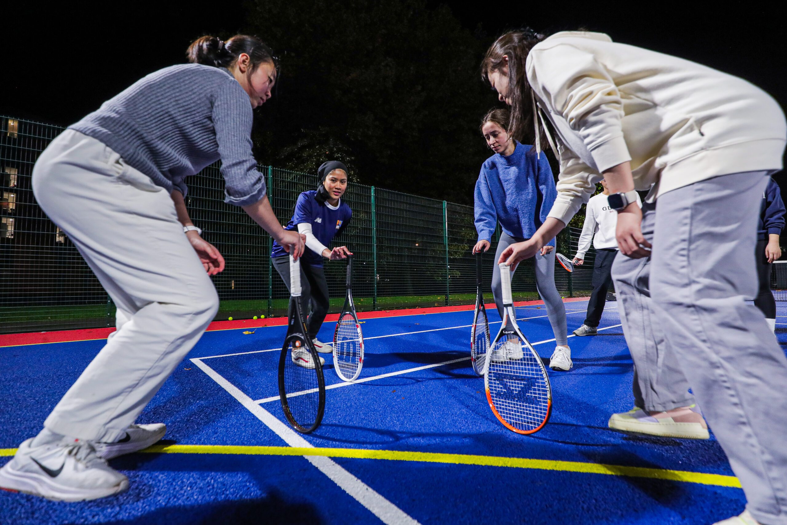 Four members of Active Residences taking part in tennis. They are stood in a circle and leaning on their tennis racquets.