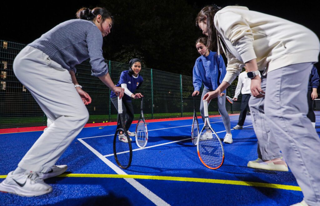 A group of four students leaning on their tennis racquets on the floor, stood in a circle.