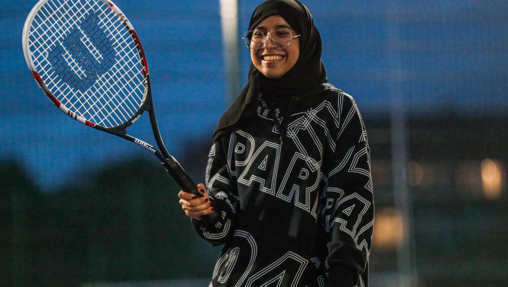 A member of active residences, smiling and holding their tennis racquet in the air.