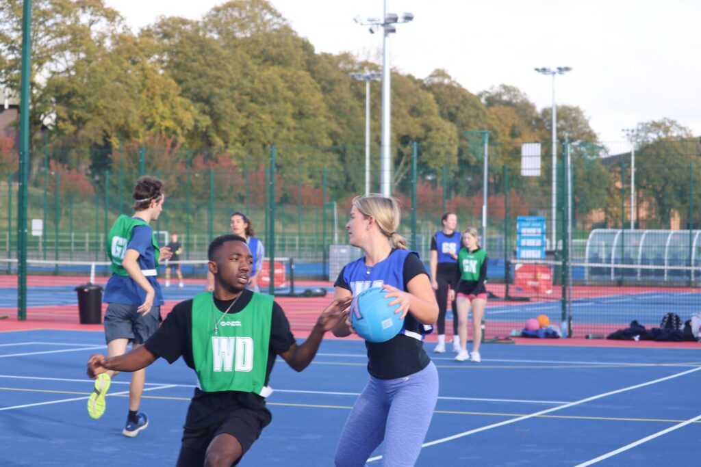 Two students playing netball on the courts at Sport & Fitness. One is holding the ball, and the other is marking.