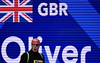 Oliver Morgan standing in front of a Great Britain sign wearing a swim cap and goggles.
