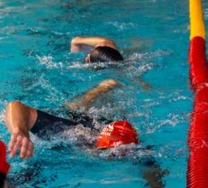 Two swim club members submerged under water. University of Birmingham swim caps on show above the water.