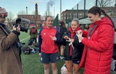Three women from Rugby team taking diagnostic swab out of packaging, with BBC videographer filming