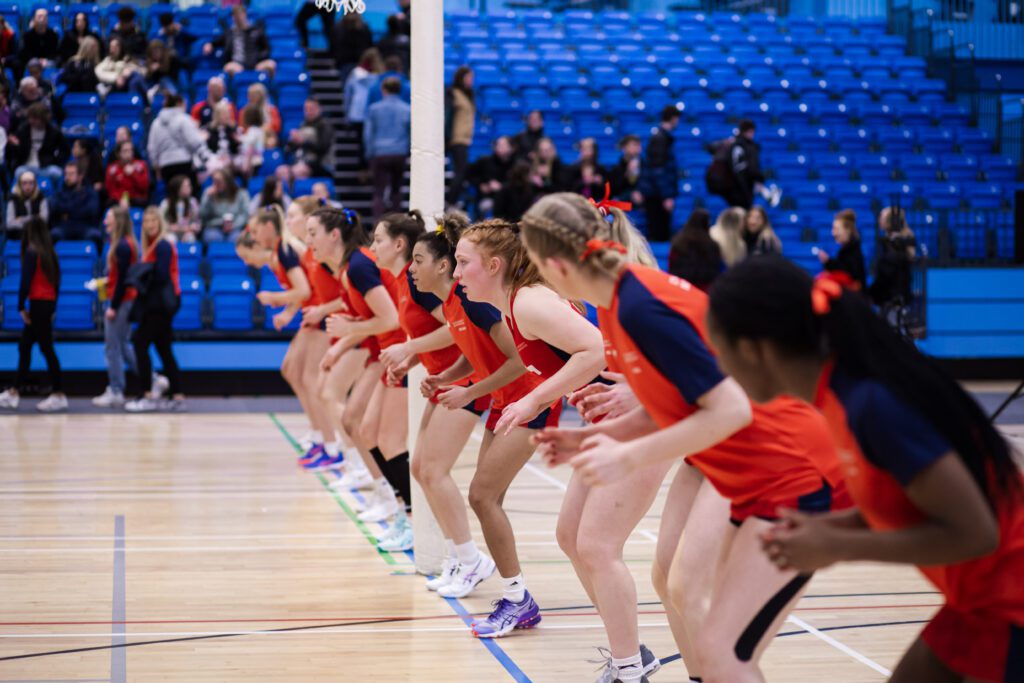 Members of the netball team all lined up on the back line, crouching and ready to run.