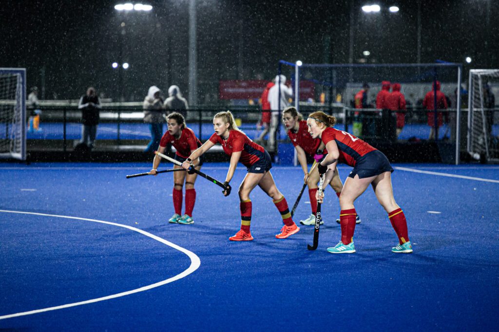 Four women playing hockey on Sport & Fitness pitches in the rain.