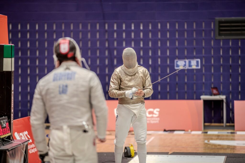 Two fencing participants dressed in fencing attire.