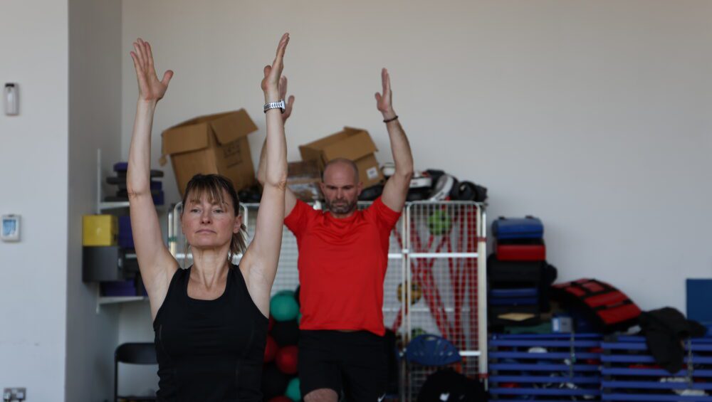 Man and woman taking part in Hatha Yoga class with hands reaching up to ceiling