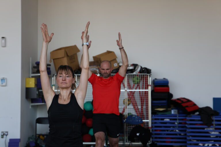 Man and woman taking part in Hatha Yoga class with hands reaching up to ceiling