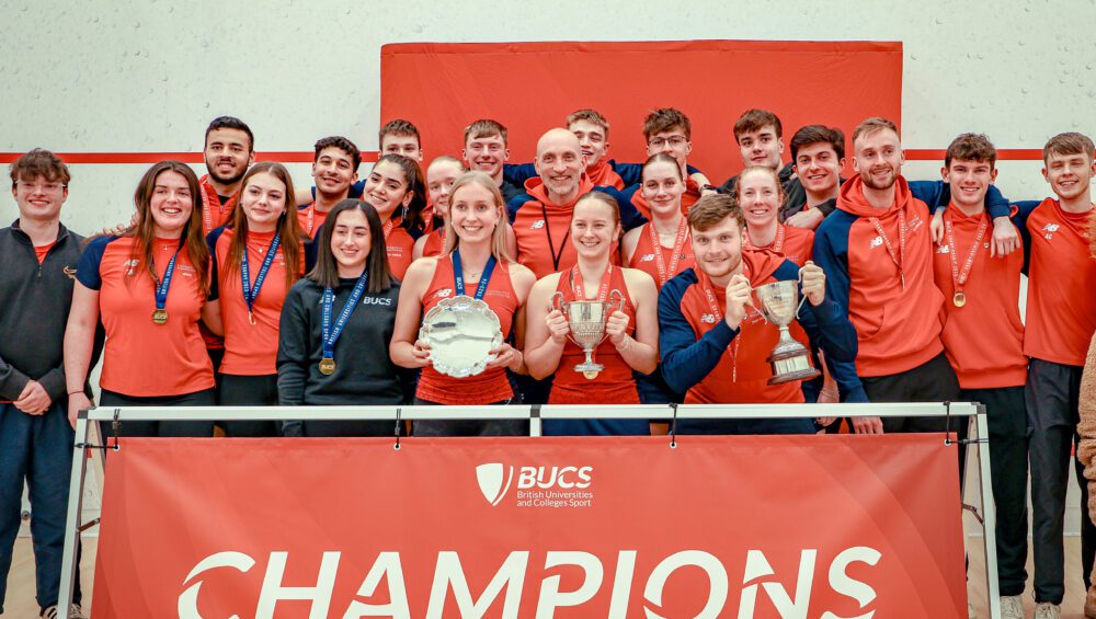 Men's and Women's Squash club winners hold trophy and stand behind Champions sign