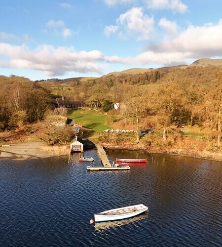 Image of the jetty at the Raymond Priestley Centre, with a boat in the Lake, and greenery surrounding it.