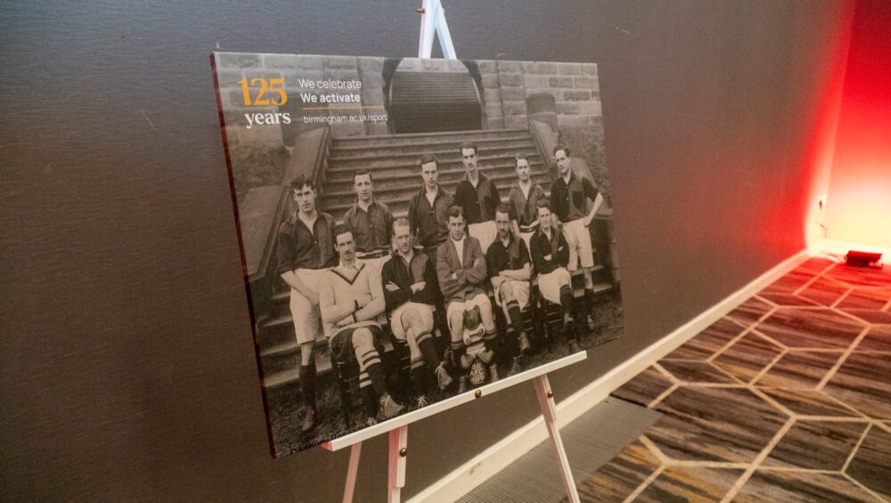 An image of a canvas printed with an old photo of the football team in black and white, balanced on an easel.